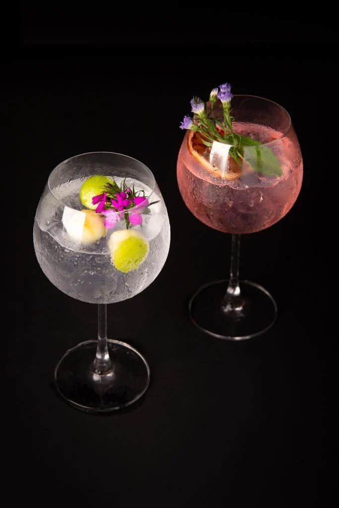Two gin cocktails garnished with edible flowers